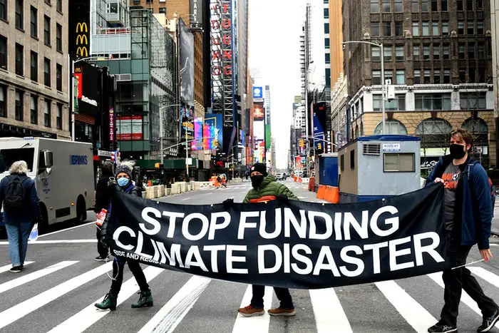 Activists wearing face masks hold a banner reading "STOP FUNDING CLIMATE DISASTER" in a Manhattan crosswalk.